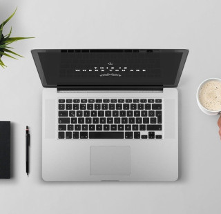 Viherkasvi, muistikirja, kynä, kannettava tietokone ja käsi, jossa kahvikuppi