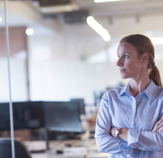 Nainen seisoo toimistossa ja katsoo sivuun kamerasta