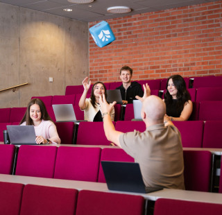 Luentosali, jossa opiskelijoita. Heittomikki ilmassa.