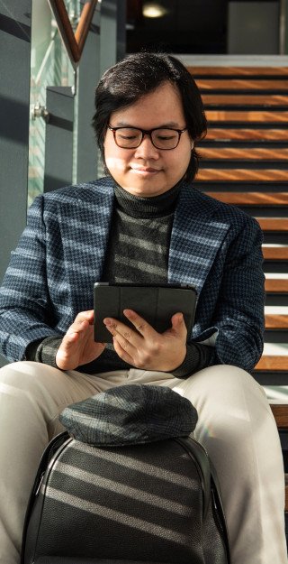 Young man sitting on the stairs, looking at the tablet device in his hands.